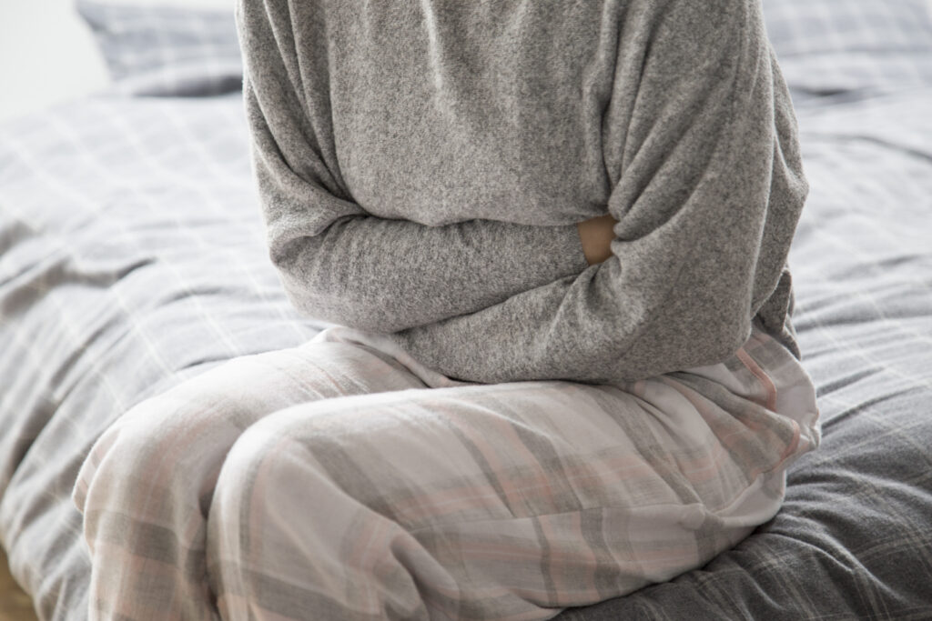 crohn's woman setting on bed while holding her stomach