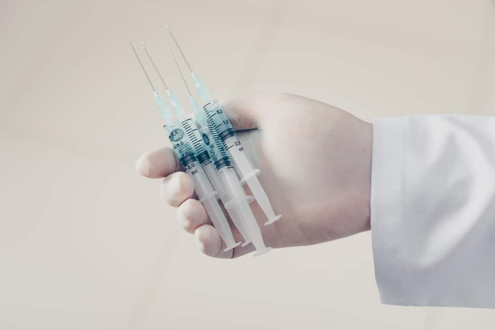 A gloved hand in a white medical coat holds three syringes filled with liquid against a plain background for infusion care planning milford delaware.