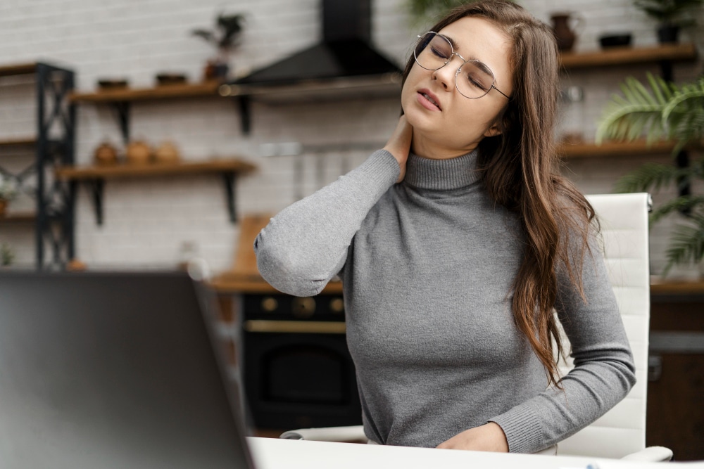 A woman working at her desk gently holds her neck, showing visible discomfort, a relatable moment for those seeking chronic pain management dover delaware to relieve daily aches and improve comfort.